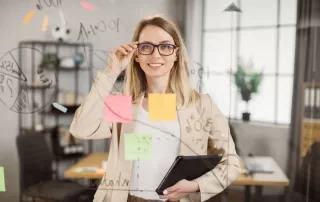 Project manager with glasses and carrying a laptop, smiling through perplex glass