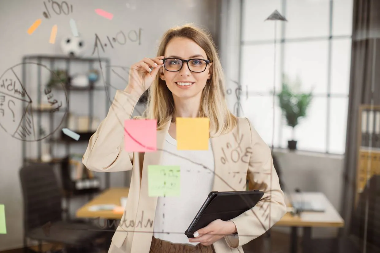 Project manager with glasses and carrying a laptop, smiling through perplex glass